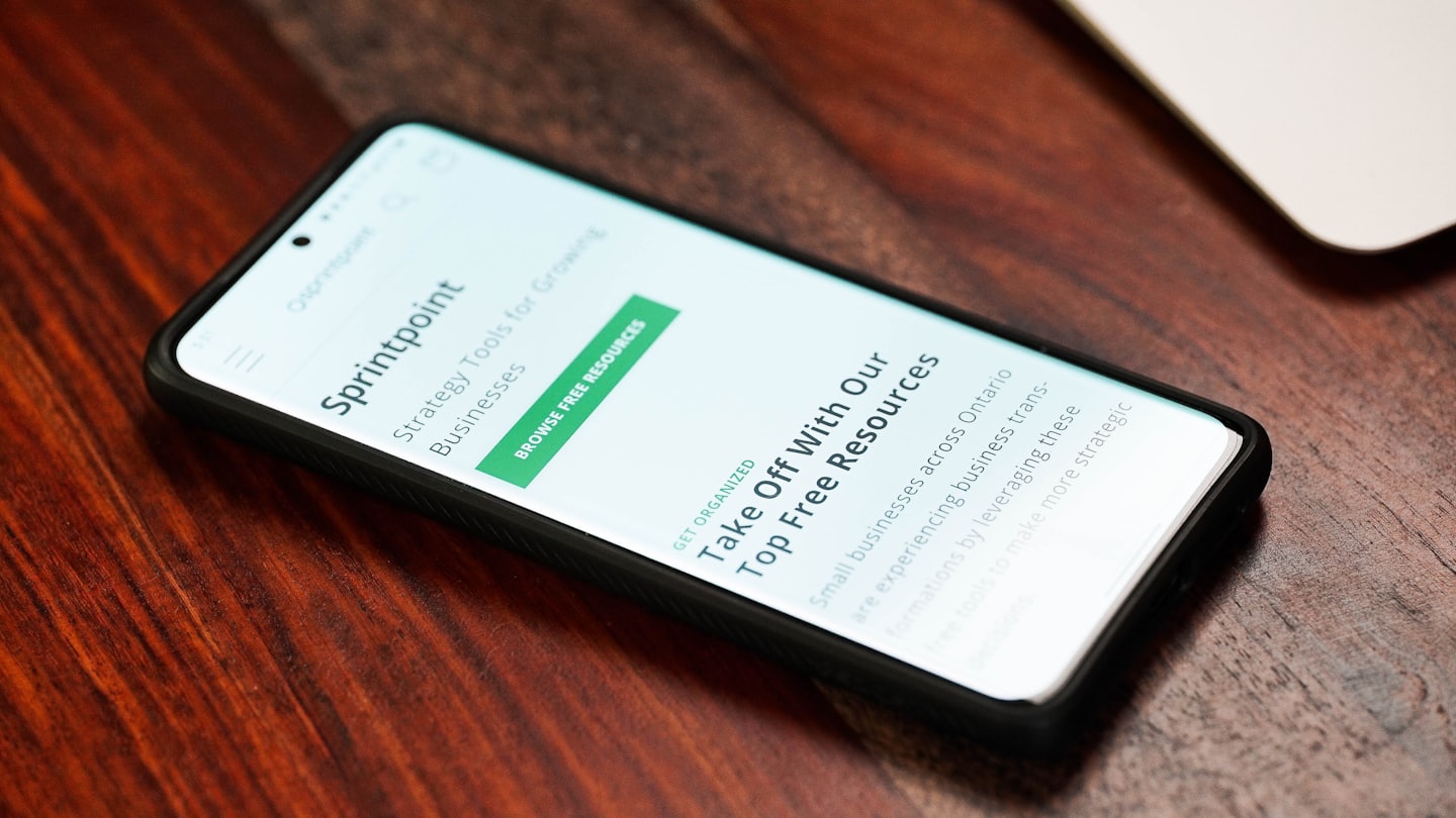 Smartfon wyświetlający stronę biznesową Sprintpoint na drewnianym stole.